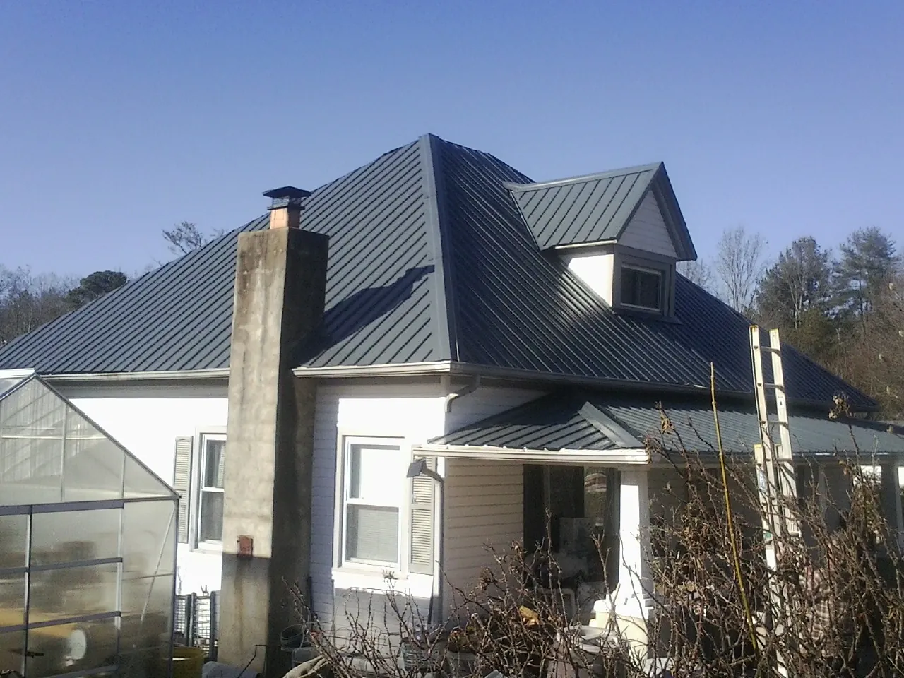 Dark blue standing seam metal roof on a white farmhouse with dormer — Slate & Tile Roof Repair by Roofing Brothers in Proctor