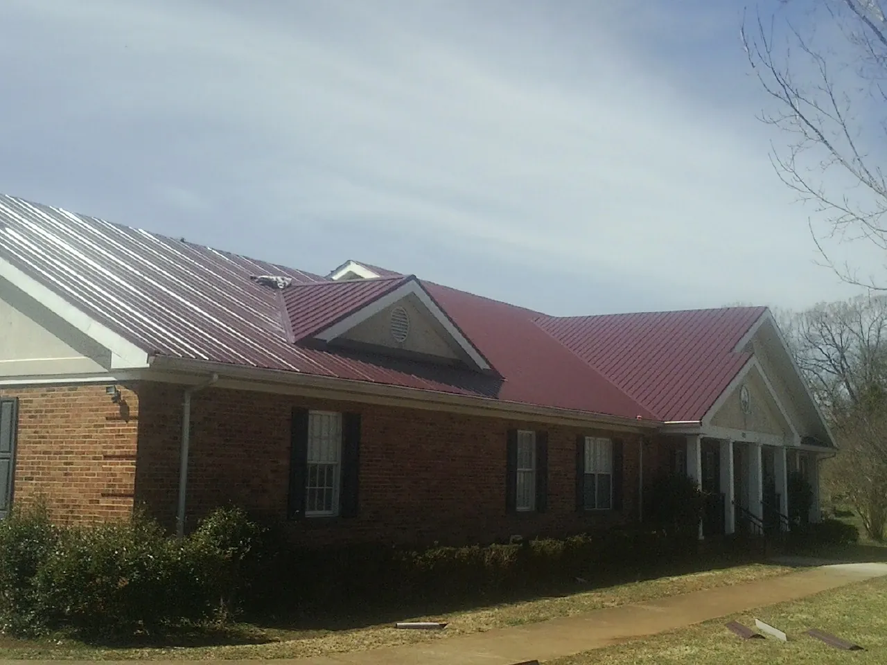 Red metal roof with gabled entries on a long brick building, from a Hail Damage Roof Repair job in Proctor