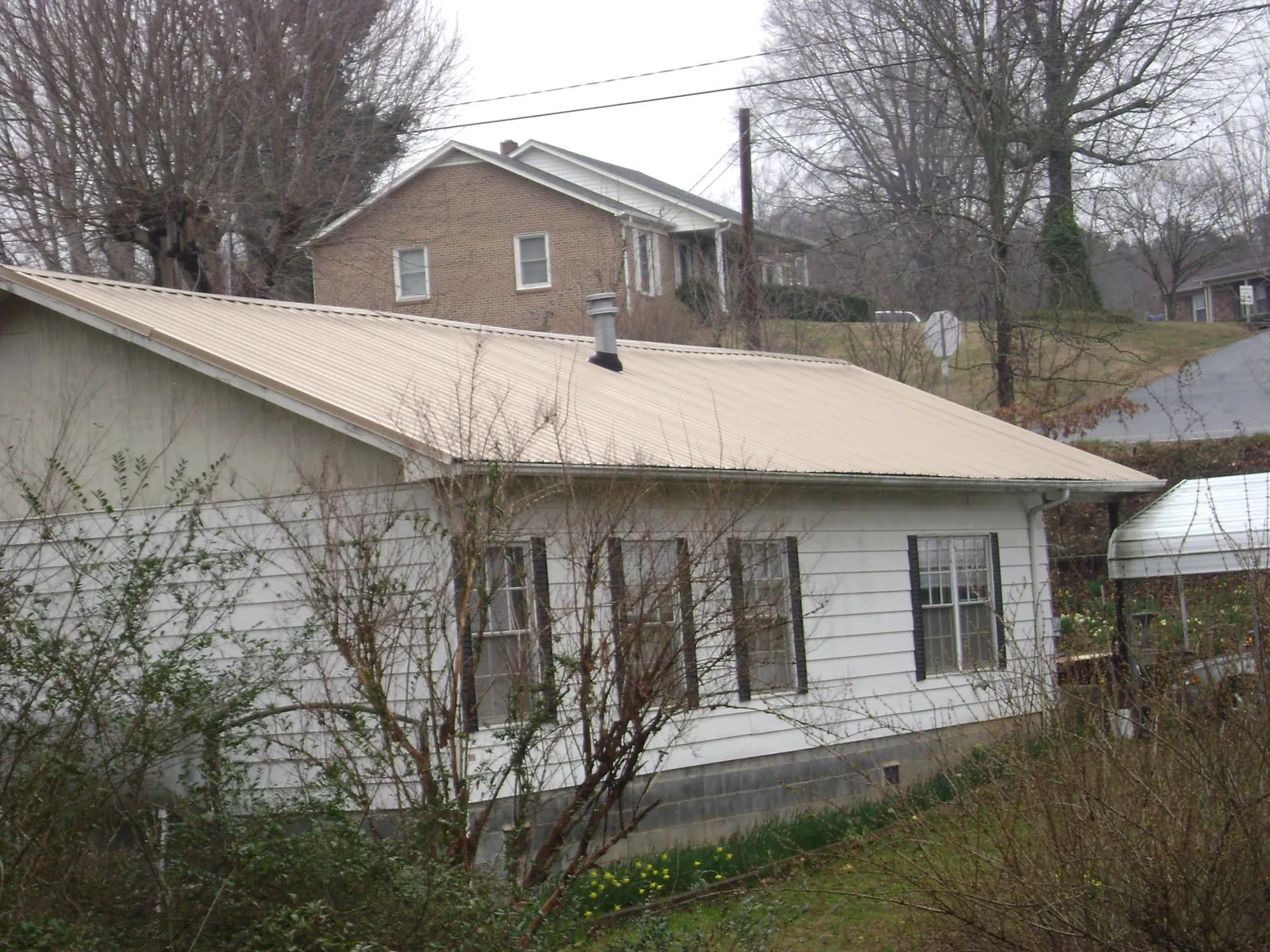 Tan metal roof on a white sided house set into a hillside — Commercial Roofing by Roofing Brothers in Proctor