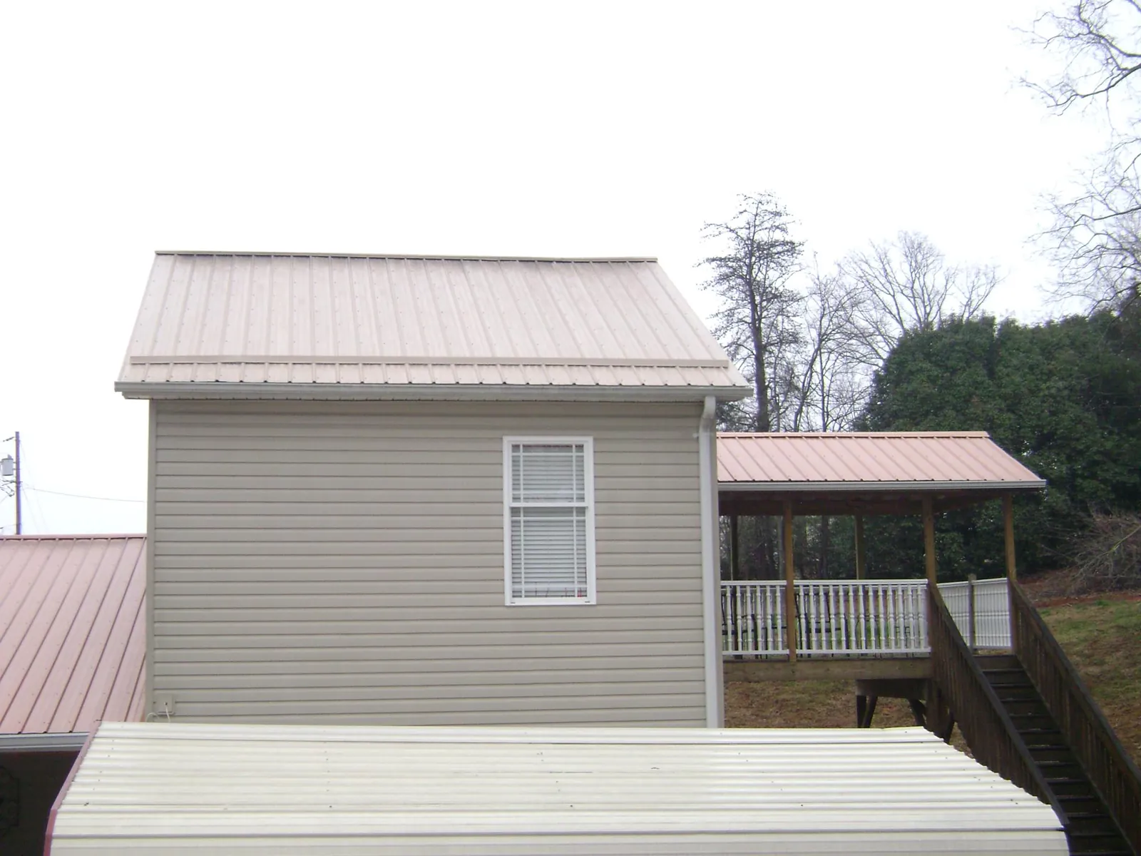 Tan metal roofs on a two story addition and attached porch, from a Roof Replacement job in Proctor